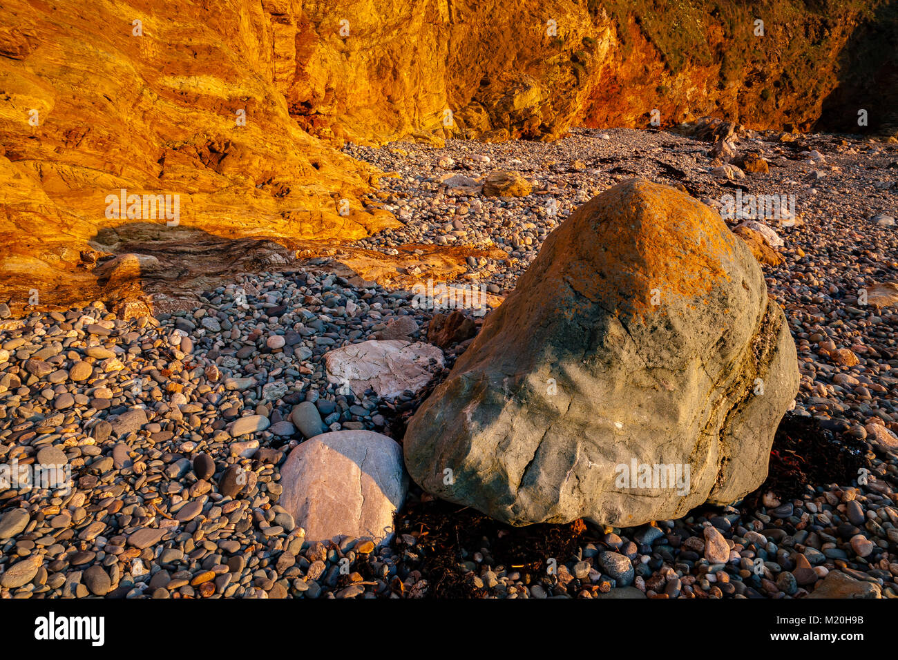 Golden cliffs, pebbles and rocks at Church Bay, Anglesey, Wales in summer sunshine Stock Photo