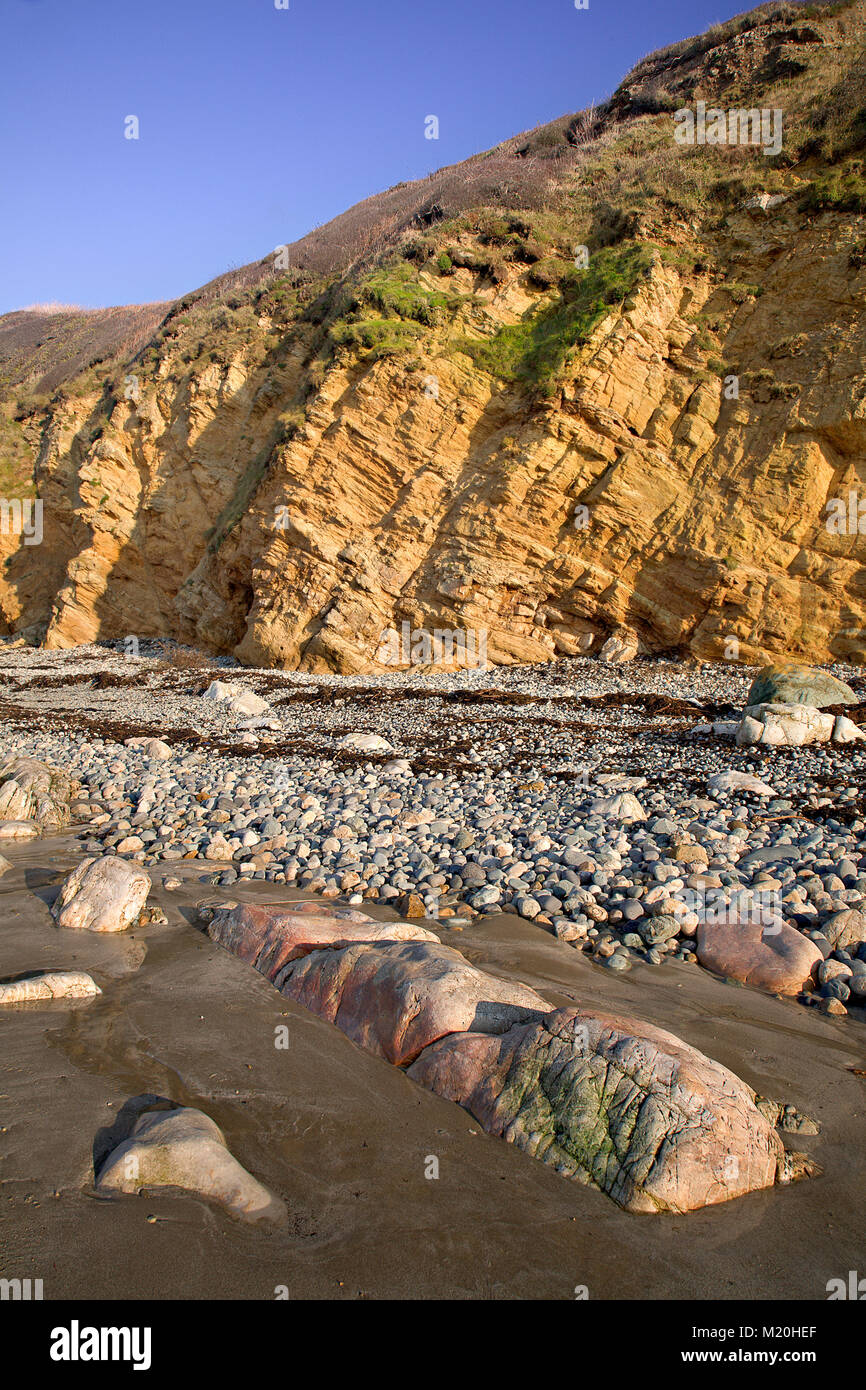 Colourful rocks, pebbles and cliff under blue skies at Church Bay, Anglesey, North Wales Stock Photo