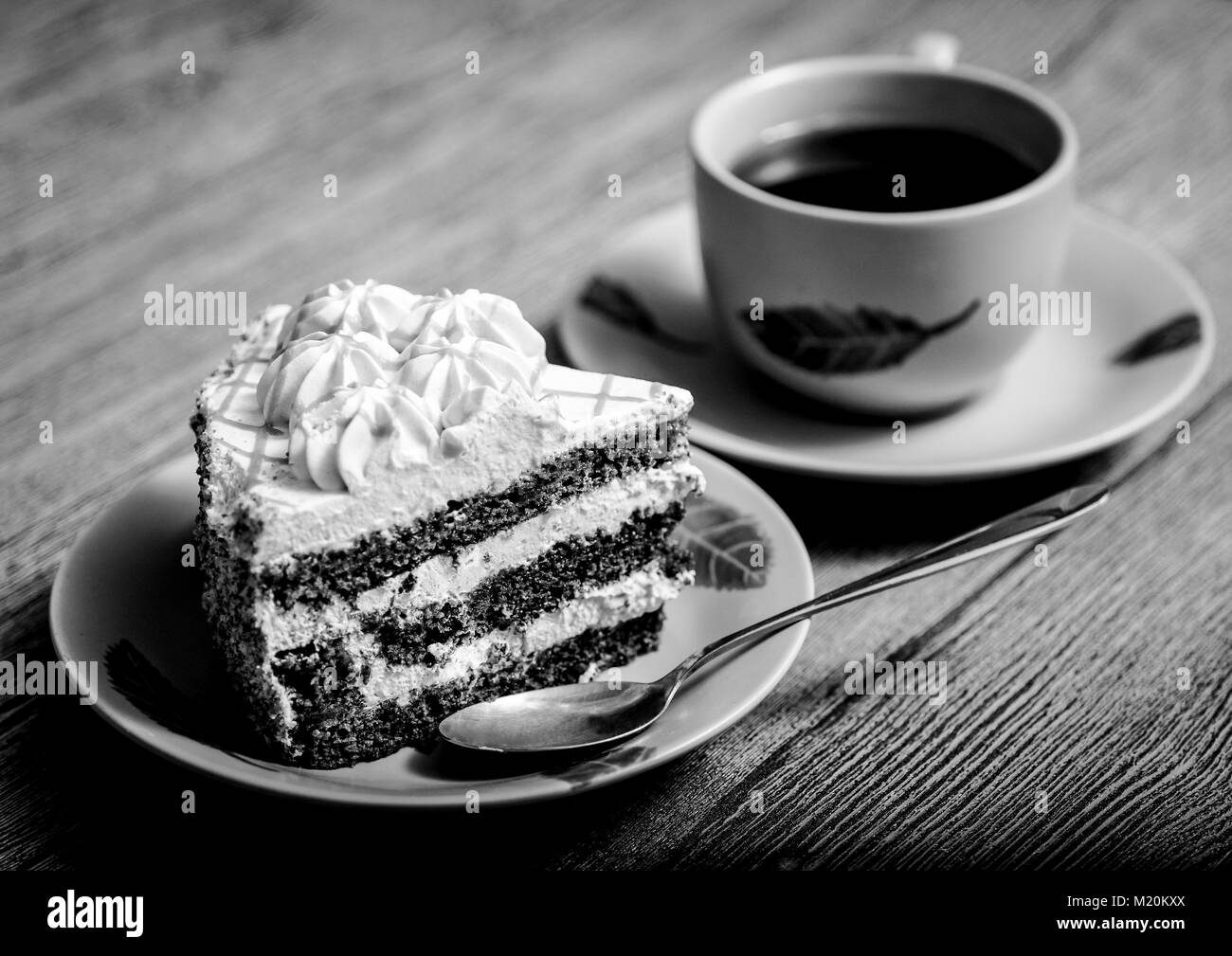 Black-and-white photo. On a wooden table plate with cake, tea Cup and spoon Stock Photo