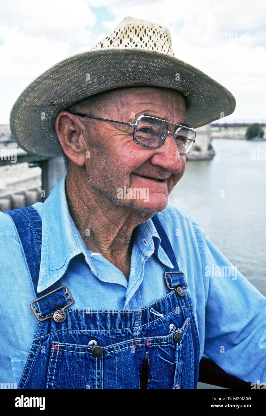 An elderly farmer wearing overalls and a straw hat, on his cotton farm