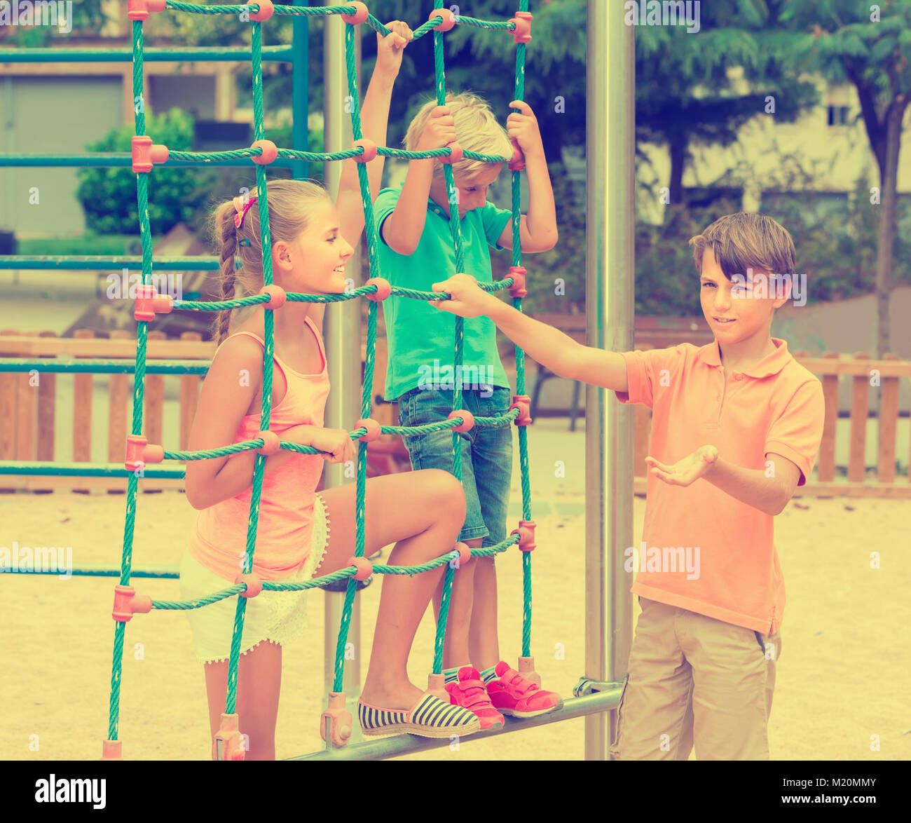Cheerful spanish children are climbing on the grid on the playground