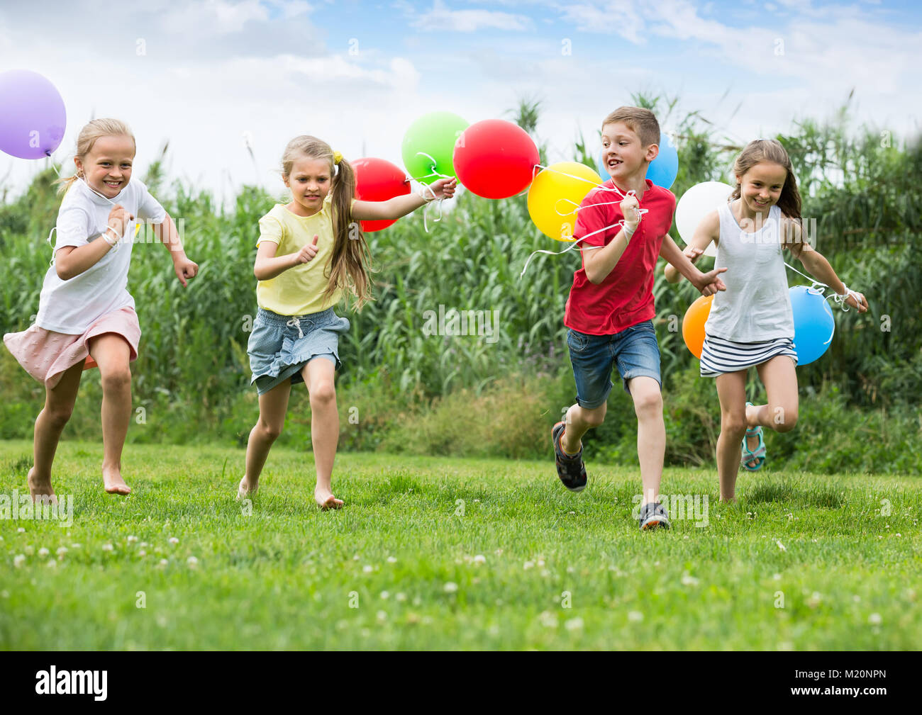 playful elementary school age boy and girls holding air balloons and ...