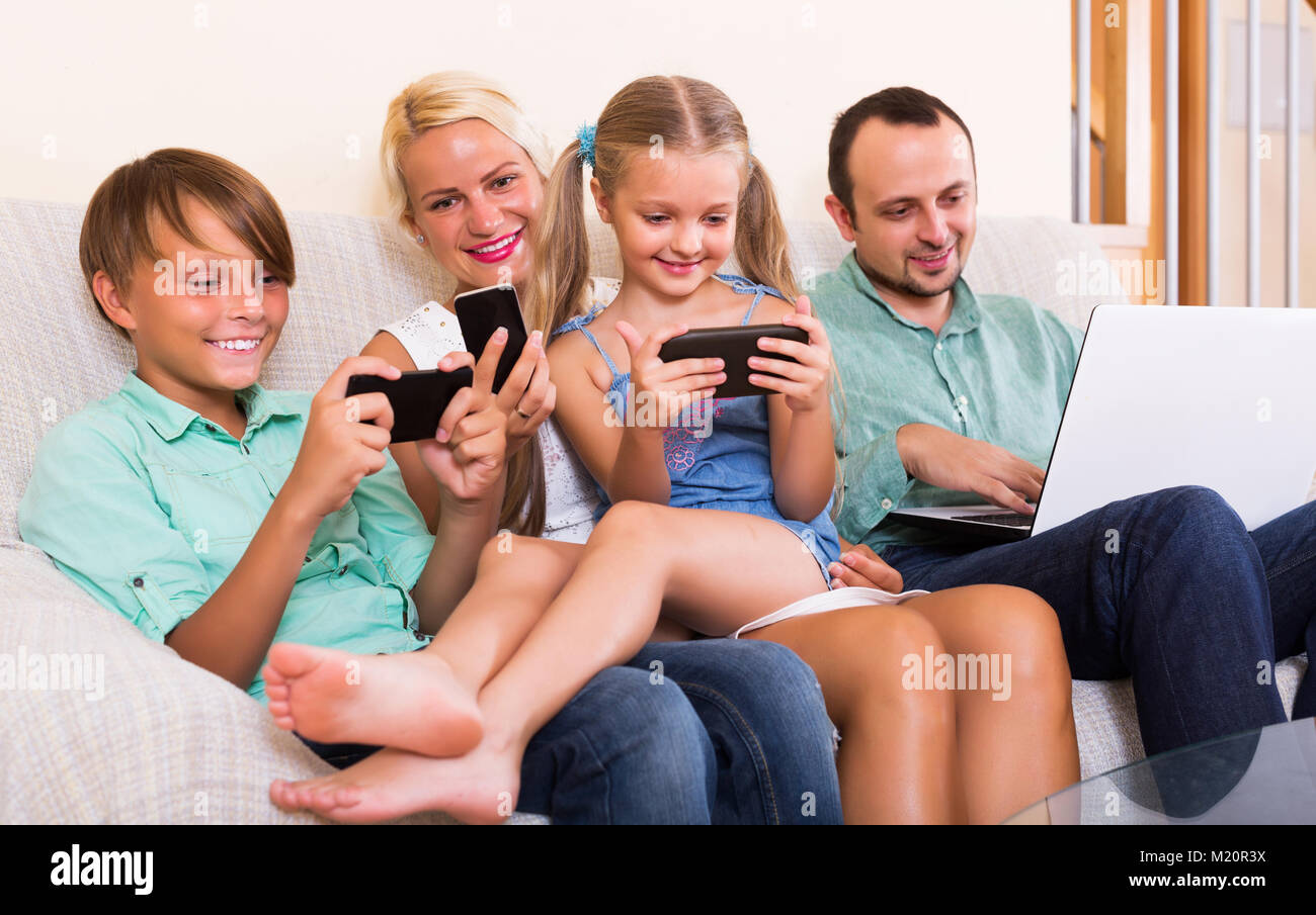 Smiling mom, dad and two happy kids working with smartphones indoors ...