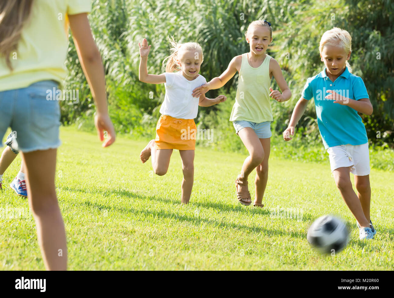 Energetic children running with ball on meadow outdoors