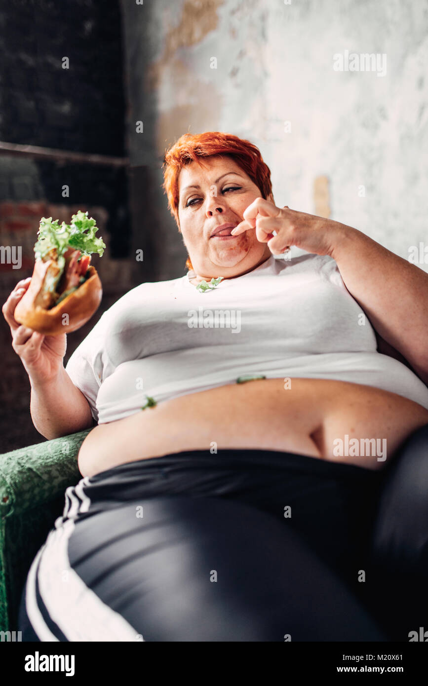 Fat woman sits in a chair and eats sandwich, overweight, fatty and bulimic. Unhealthy lifestyle, obesity Stock Photo