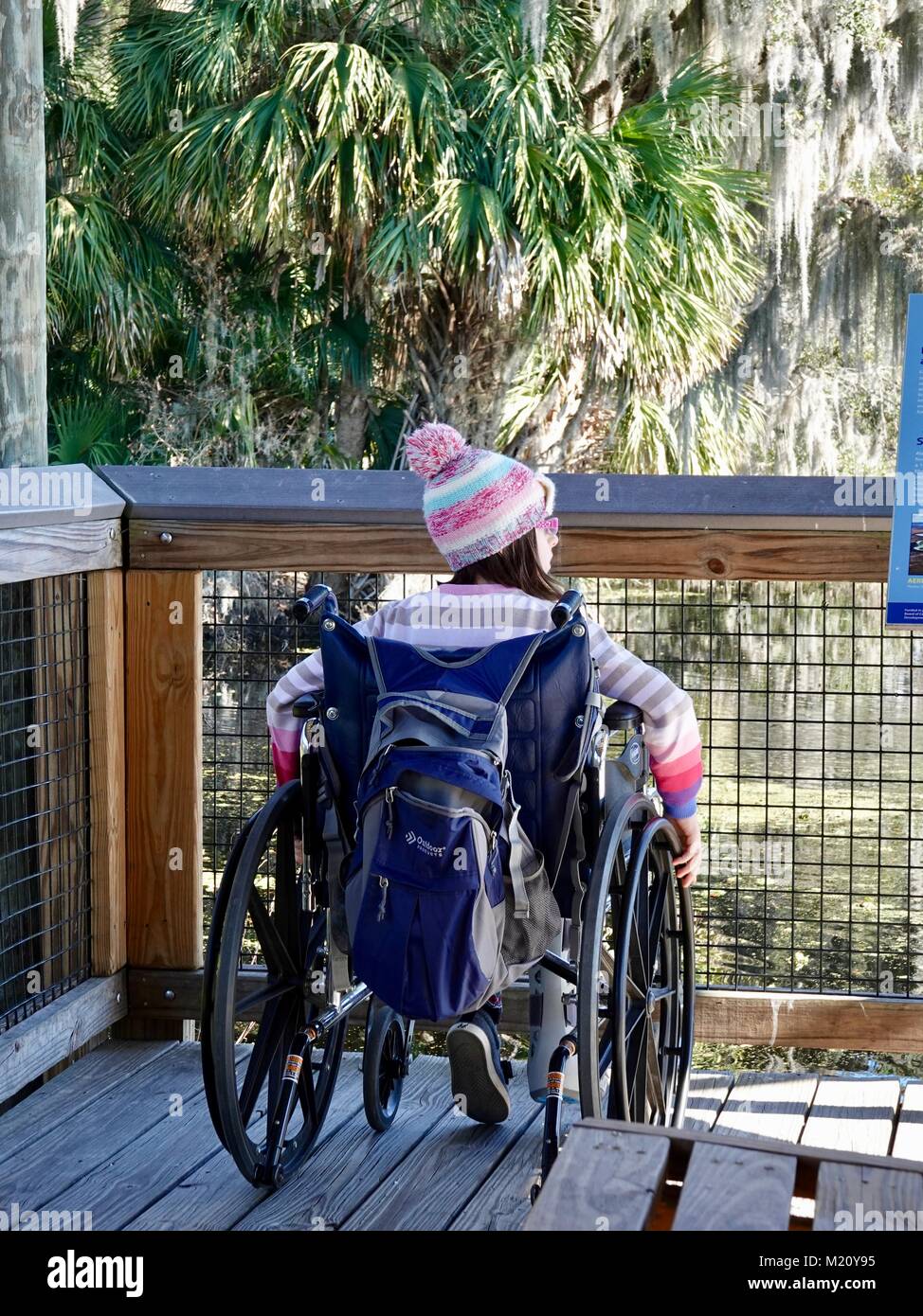 Girl sitting in wheelchair, enjoying nature, on boardwalk of Paynes Prairie Preserve State Park