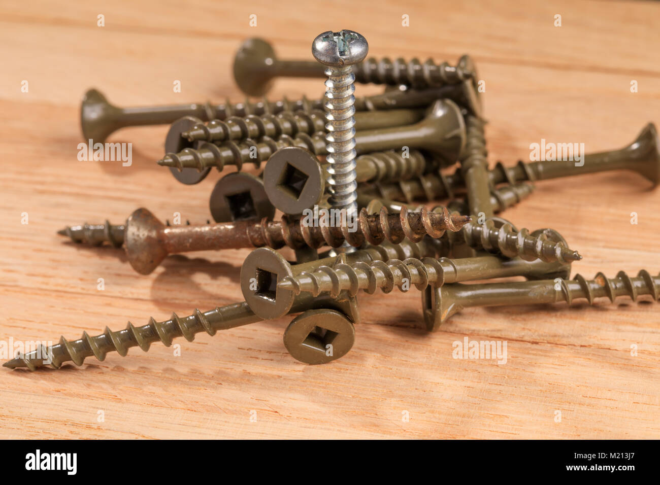 Used screws for construction projects on a wooden board background. Screw that is installed up in place, along with other used screws. Stock Photo