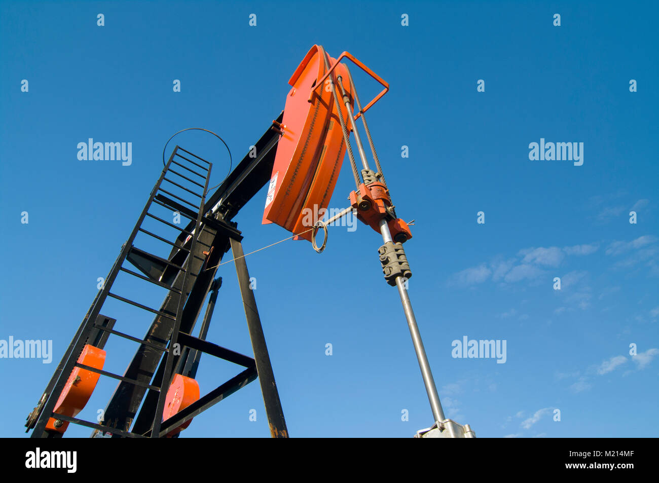 Looking up at an angle at the horsehead of an oil well pumpjack against a blue sky Stock Photo