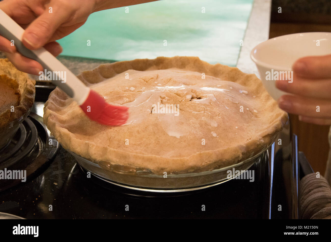 Homemade apple pie in a glass pan on a stove top being prepared by a