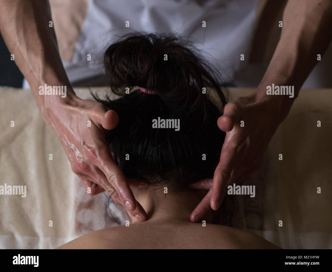 Beautiful young woman reciving relxing Massage of Her Oiled Neck from Professional Masseur Stock Photo