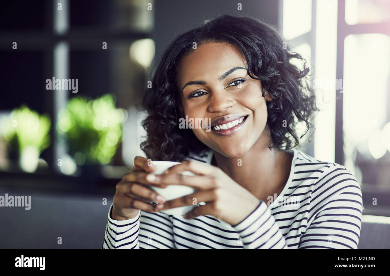 Young African woman smiling while sitting alone at a table in a cafe ...