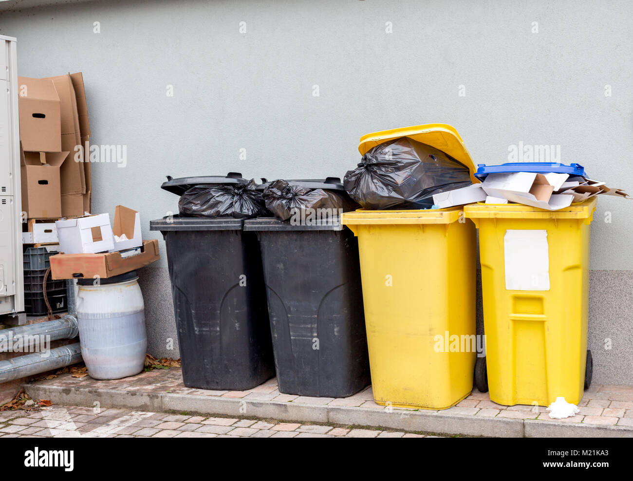 Overflowing plastic waste cans with black garbage bags, cardboard boxes and a container with a liquid Stock Photo