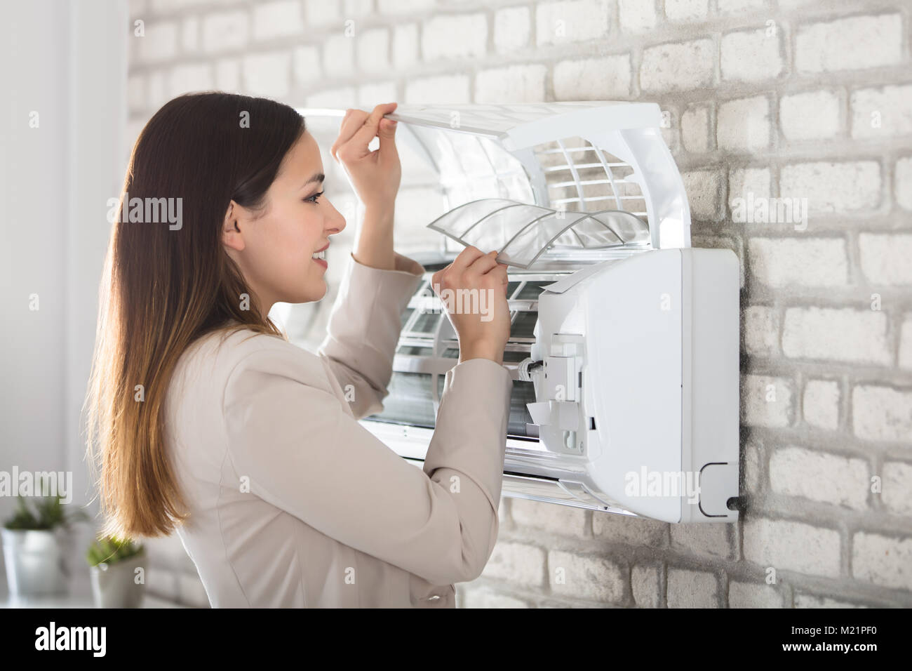 Young Smiling Woman Cleaning The Air Conditioner Attached On Wall Stock Photo