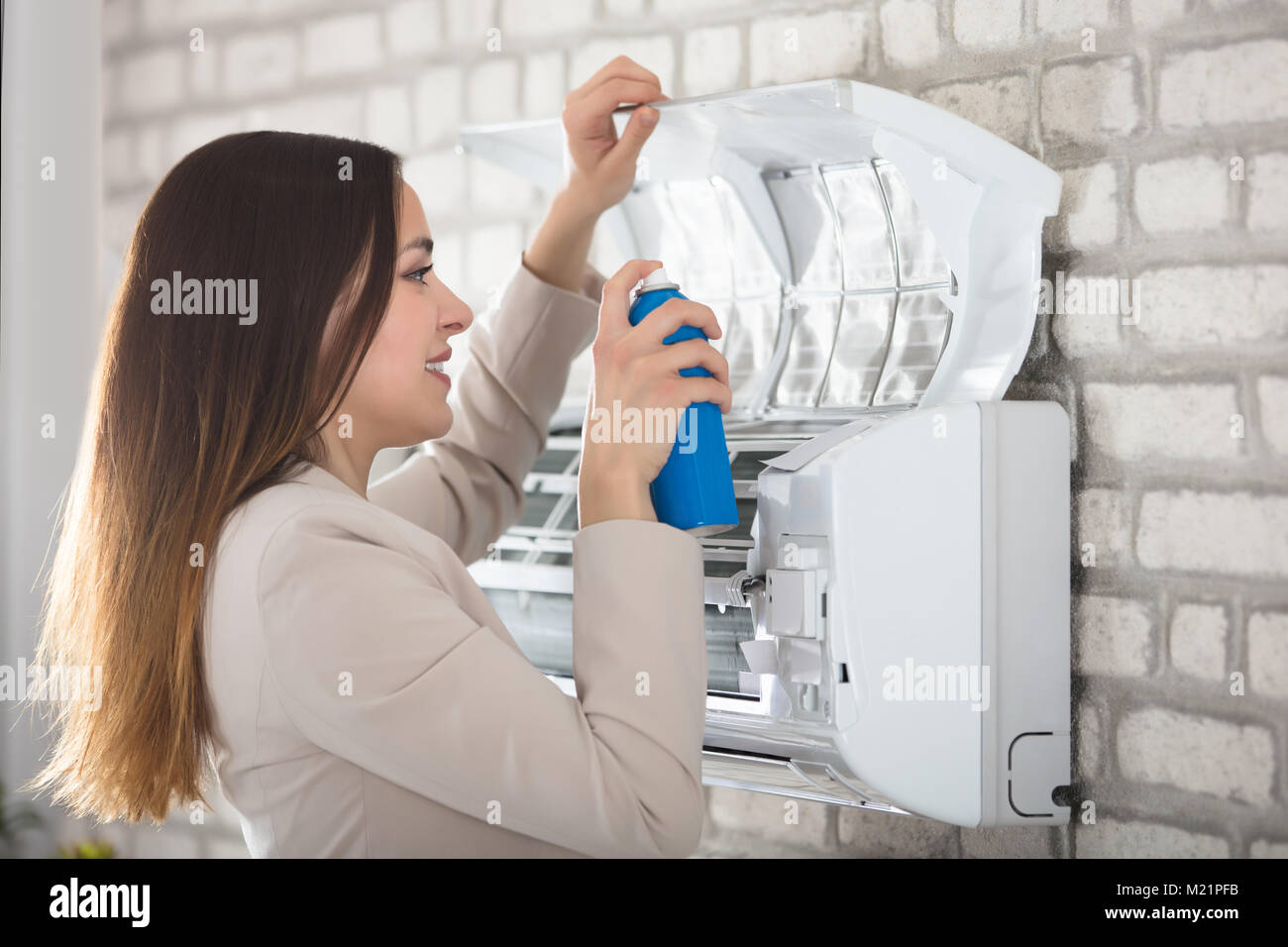Smiling Young Woman Cleaning The Air Conditioner With Spray Bottle Stock Photo