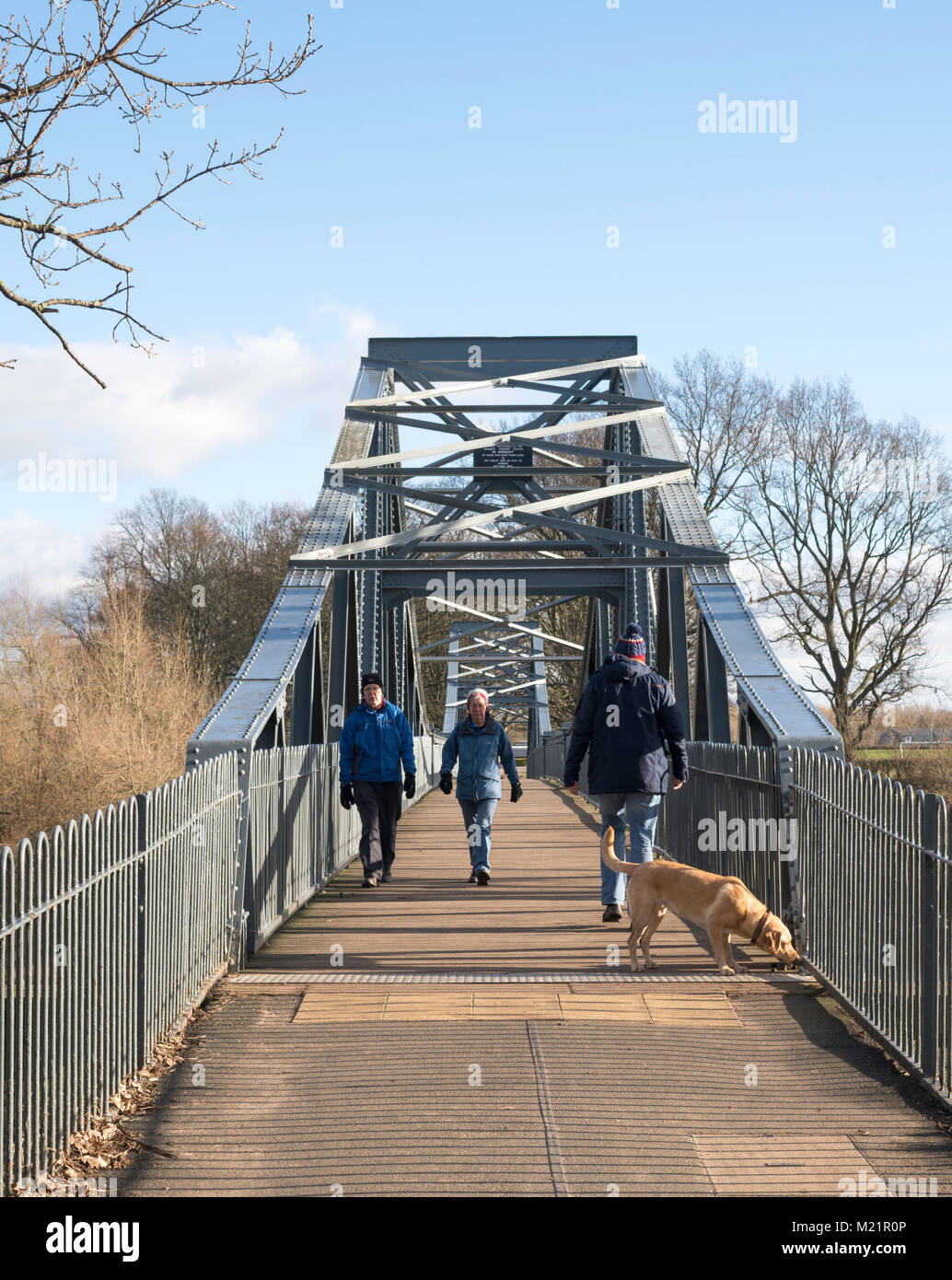 Couple with dog walking across Rickerby Park memorial footbridge over the river Eden in Carlisle, Cumbria, England, UK Stock Photo