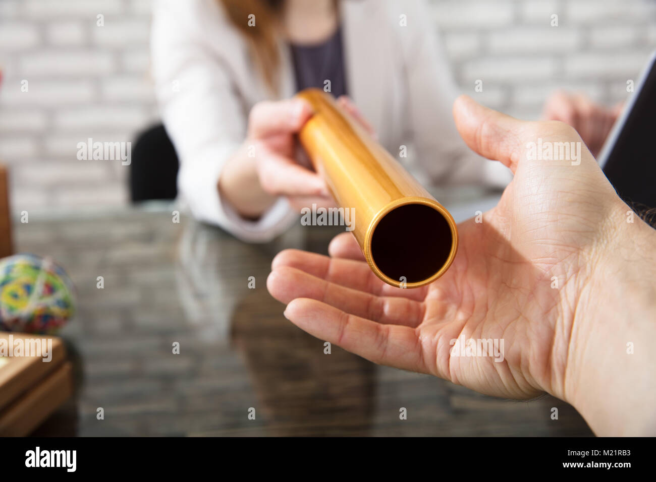 Close-up Of A Hand Passing Golden Relay Baton To Businesswoman Stock Photo