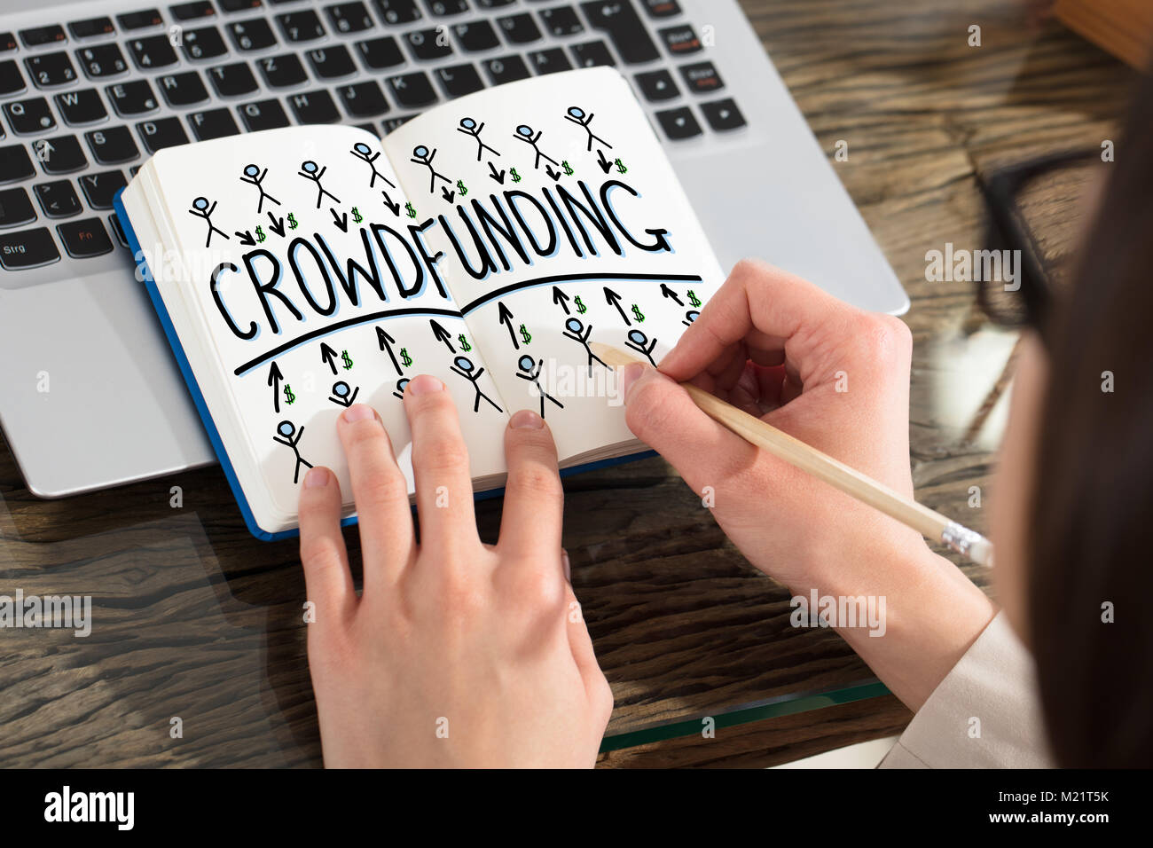 Close-up Of A Business Person Drawing Crowdfunding Chart On Notebook Over The Laptop Stock Photo