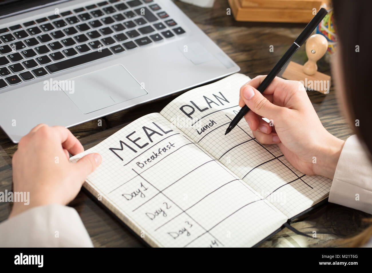Businesswoman Writing Down A Meal Plan In Checkered Notebook With Black Marker Over The Desk Stock Photo