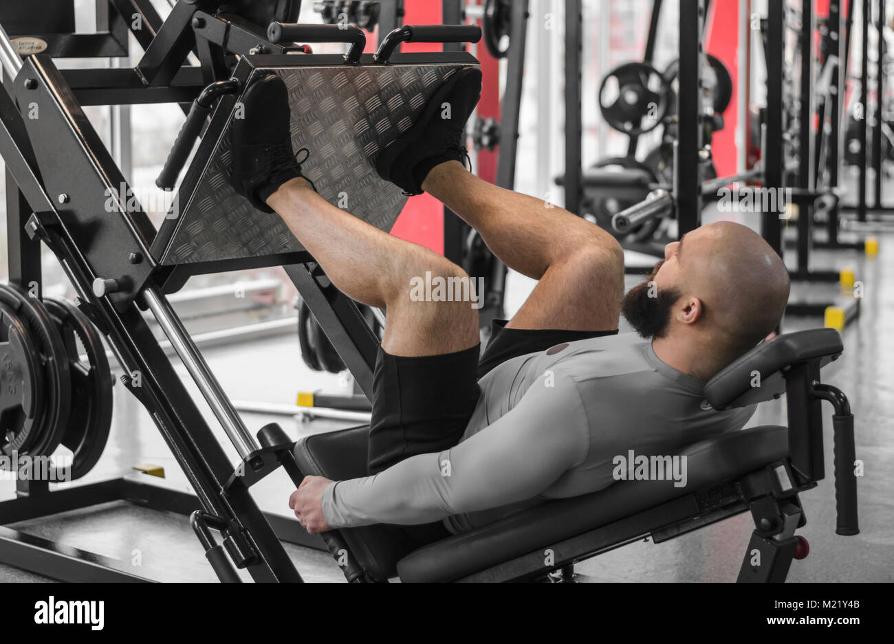 Strong man with fit muscular body doing exercises on leg press machine