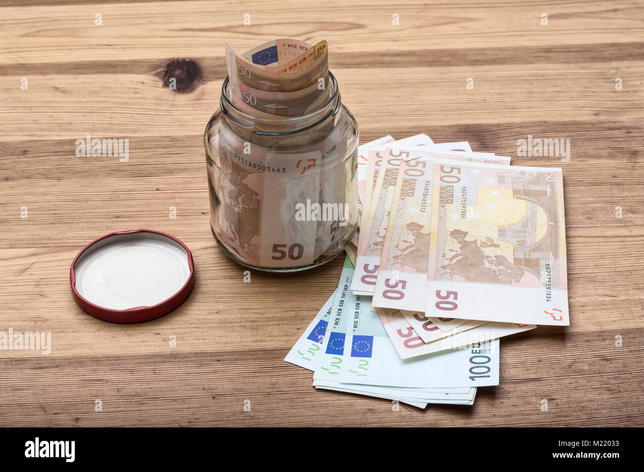 A jar of cash on the table. Next to jar a lot of euro banknotes, cash, money, concept of accumulation, finance, business, economics. Stock Photo