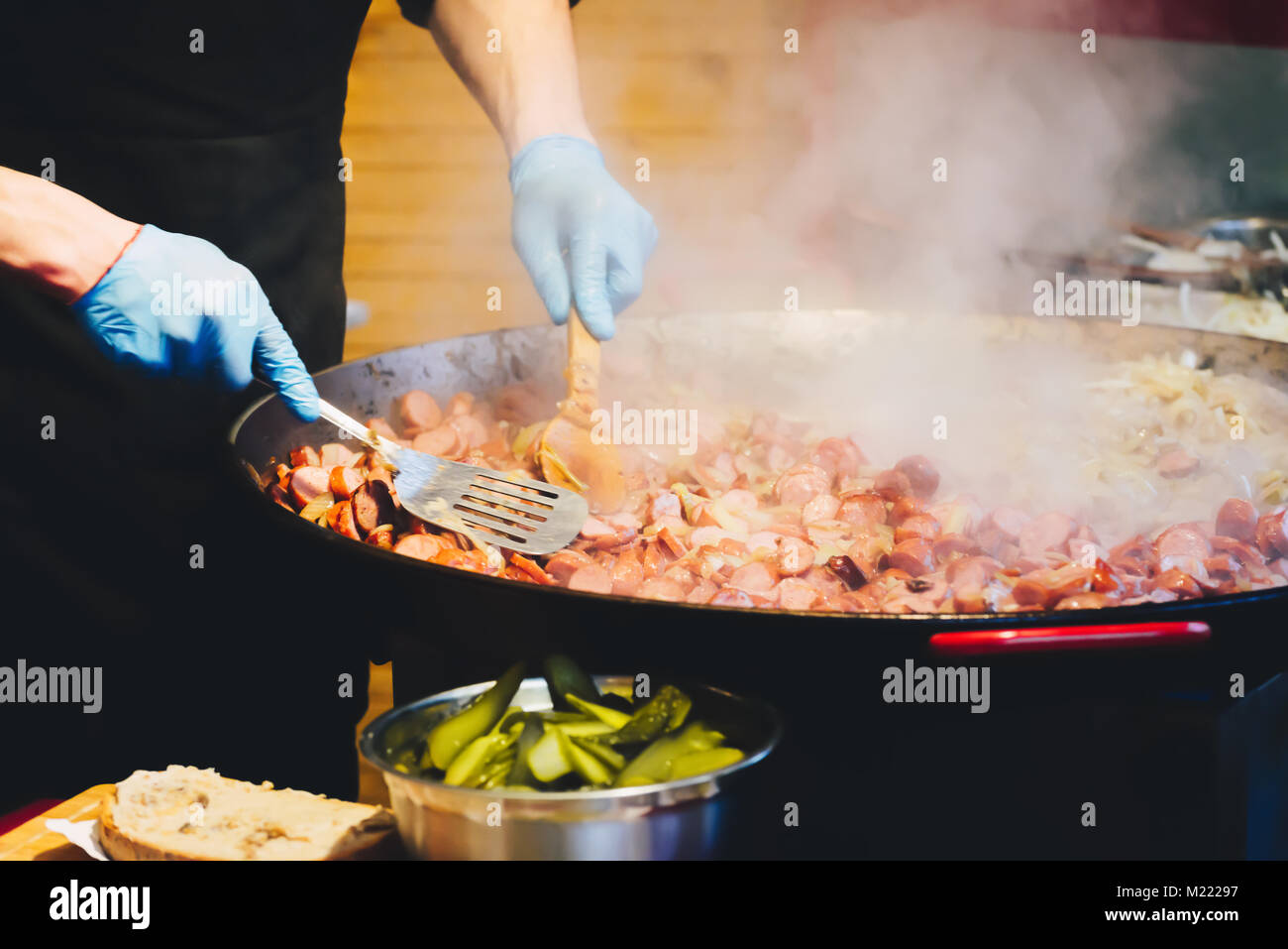 Chef cooking stew sausages in large wok at the city street. Close-up cooking process. Street food. National cuisine Stock Photo