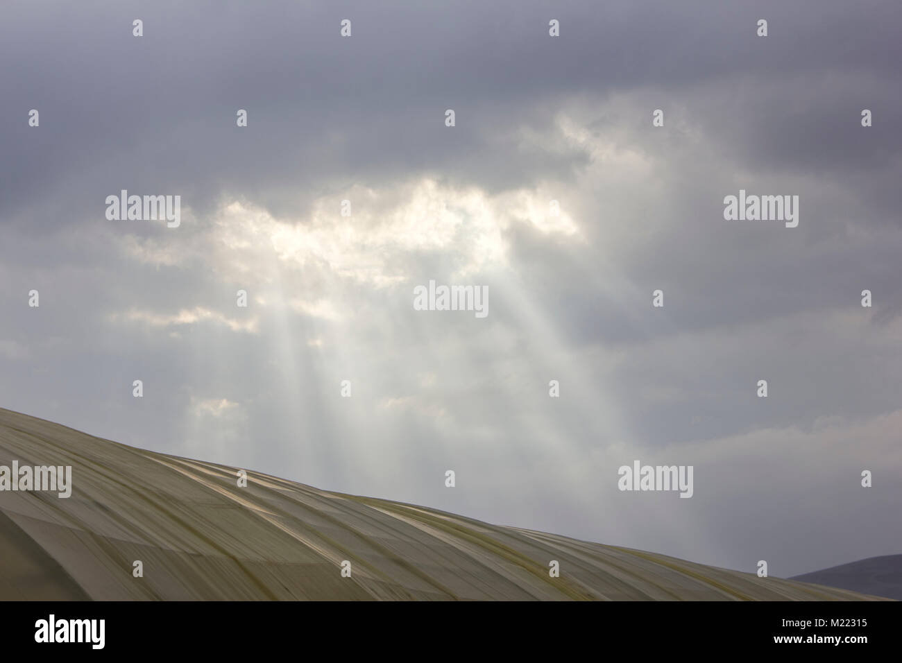 sun rays breaking through the clouds over a mountain landscape Stock Photo