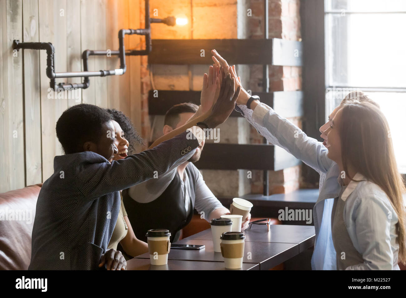 Diverse friends join hands together giving high-five at cafe mee Stock Photo