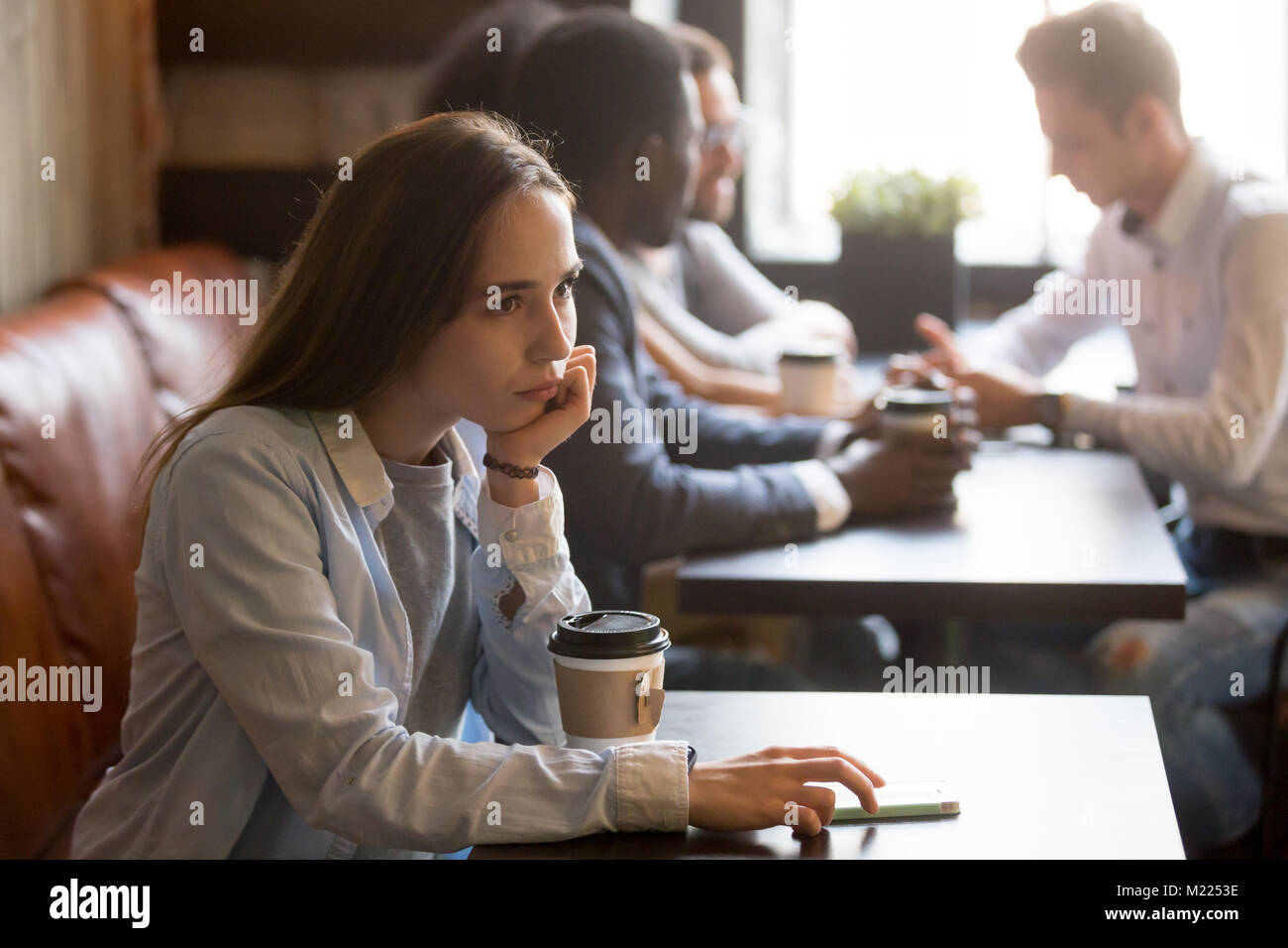 Pensive upset young girl sitting alone at table in cafe Stock Photo