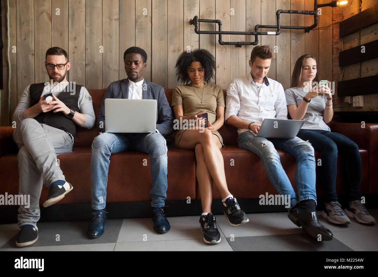Diverse young people sitting in row obsessed with devices online Stock Photo