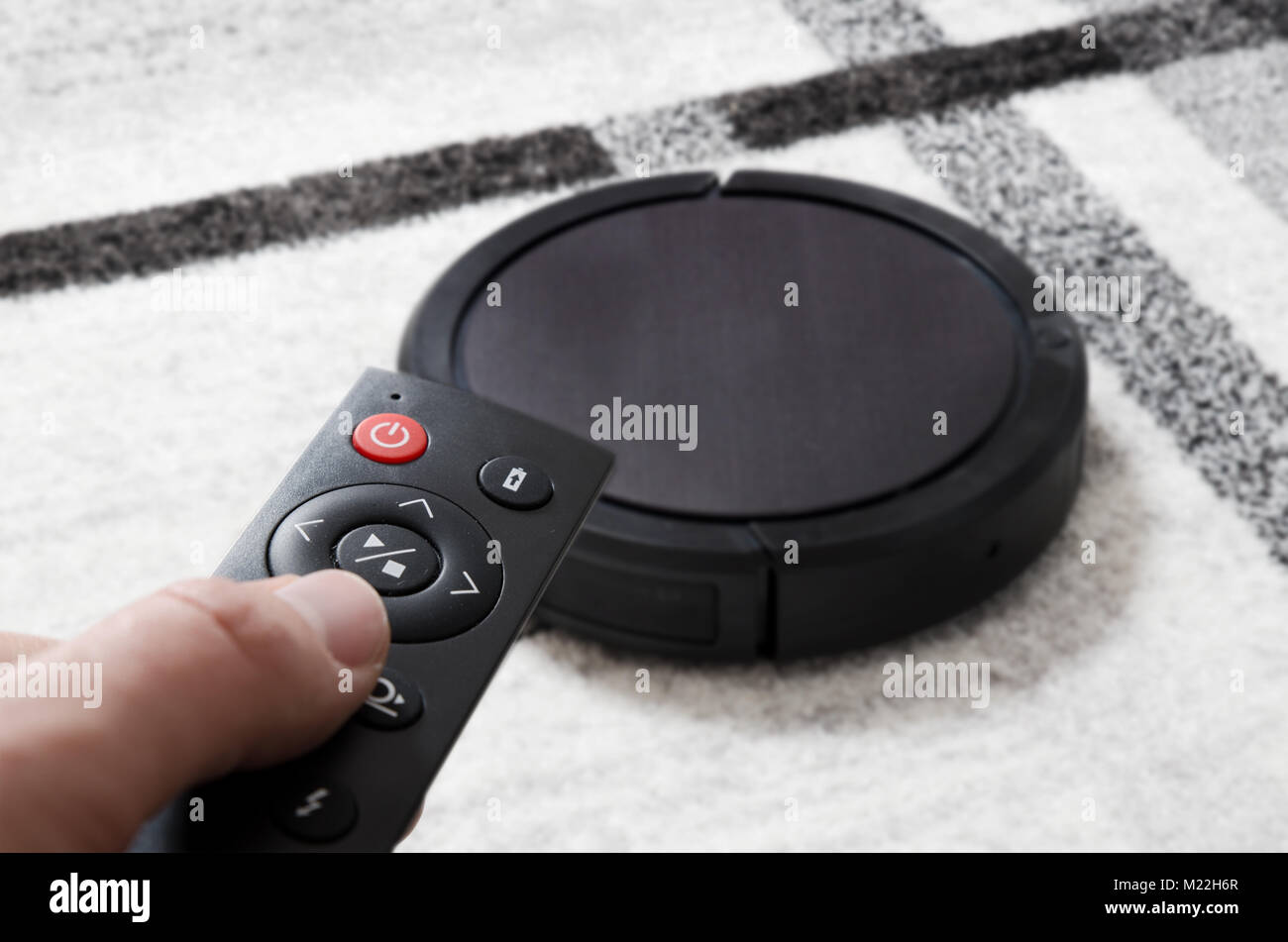 Robotic vacuum cleaner working on carpet. Hand holding remote control Stock Photo