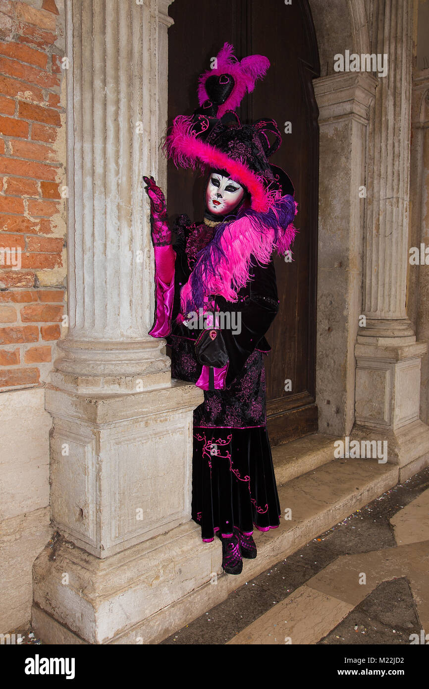 Female Venetian Mask - Cat mask in pink / black elegant costume on St. Mark's Square in Venice with traditional venetian pillar - Venice Carnival Stock Photo