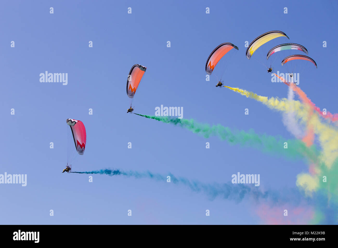 Airshow exibition of multicolored powered parachutes. Paratroopers during the air performance with trail of italian flag colors in the clear blue sky. Stock Photo