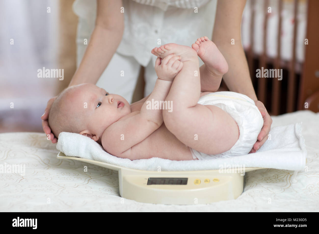 Mommy is measuring baby weigh on scales at home Stock Photo