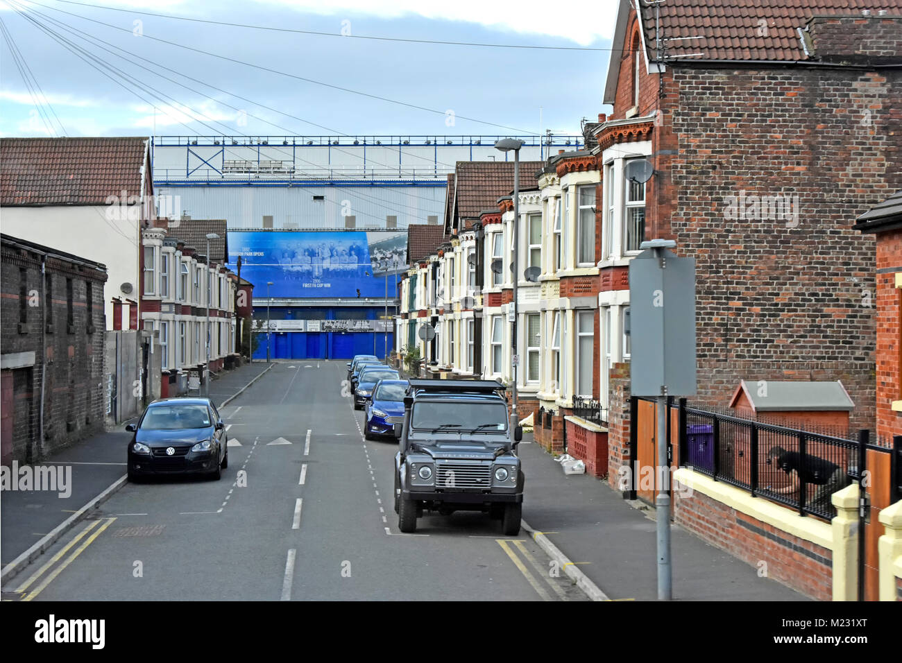 Residential Street of terraced houses with traffic calming humps & Everton football club Goodison Park stadium at end of road Liverpool England UK Stock Photo