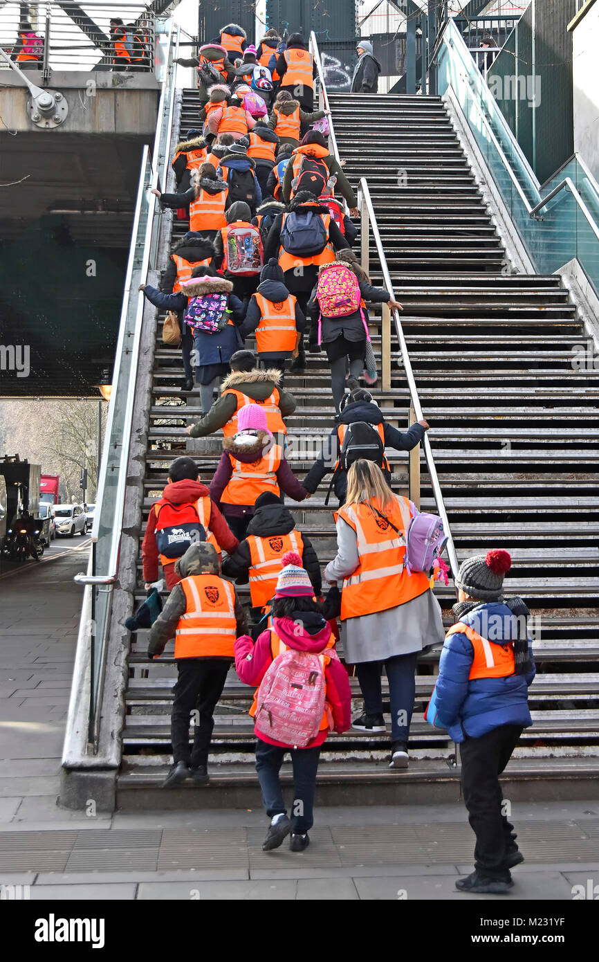 Group of primary school children in high visibility vests with teachers & assistants climbing steep steps onto footbridge crossing River Thames UK Stock Photo