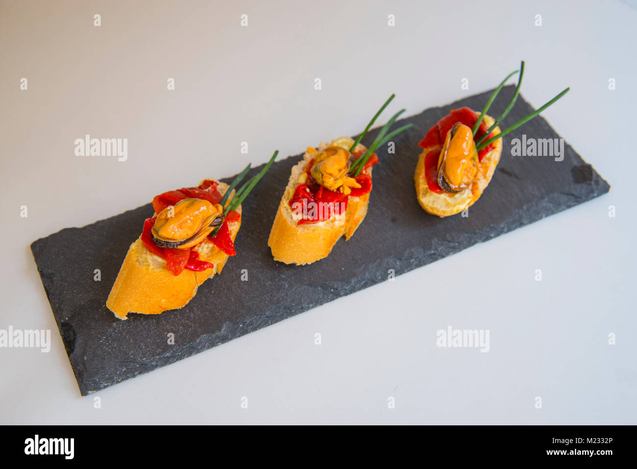 Spanish tapas mussels with red peppers and chives on toast Stock Photo