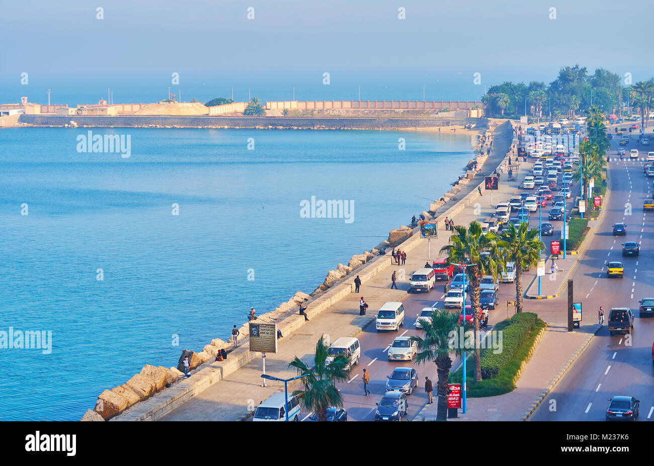 ALEXANDRIA, EGYPT - DECEMBER 17, 2017: The foggy Corniche embankment in the early morning, transport ride along the road and people walk on the seasid Stock Photo