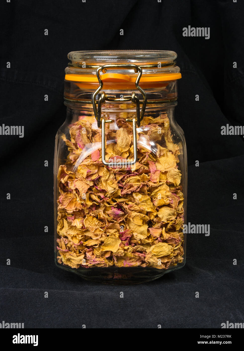 dried rose petals in a glass jar with lid on a black background Stock