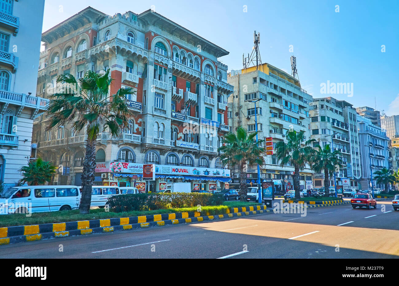 ALEXANDRIA, EGYPT - DECEMBER 17, 2017: The walk along the Corniche avenue with preserved historic mansions, beautiful palms and busy road, on December Stock Photo