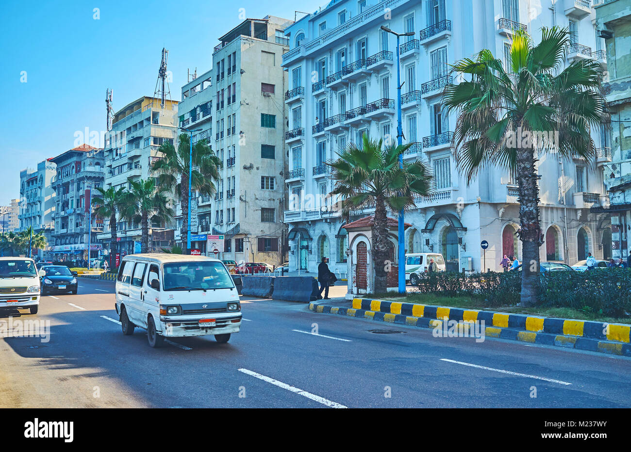 ALEXANDRIA, EGYPT - DECEMBER 17, 2017: The mini bus rides along the Corniche avenue with palm trees and Colonial style buildings on background, on Dec Stock Photo