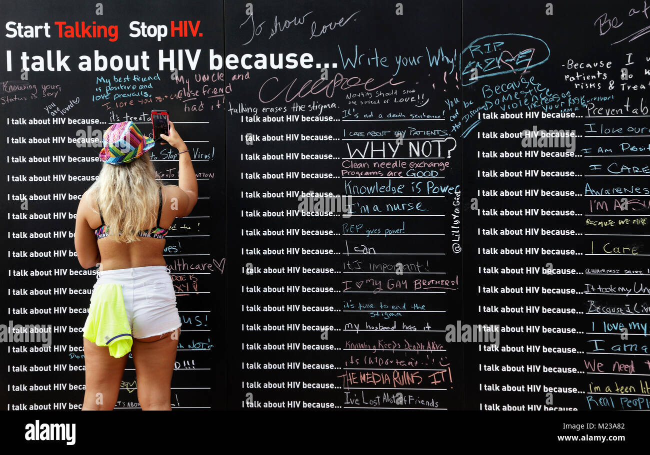 Woman taking photo of a Wall with statements about HIV awareness, 'Start talking. Stop HIV. I talk about HIV because' during Charlotte Pride festival Stock Photo