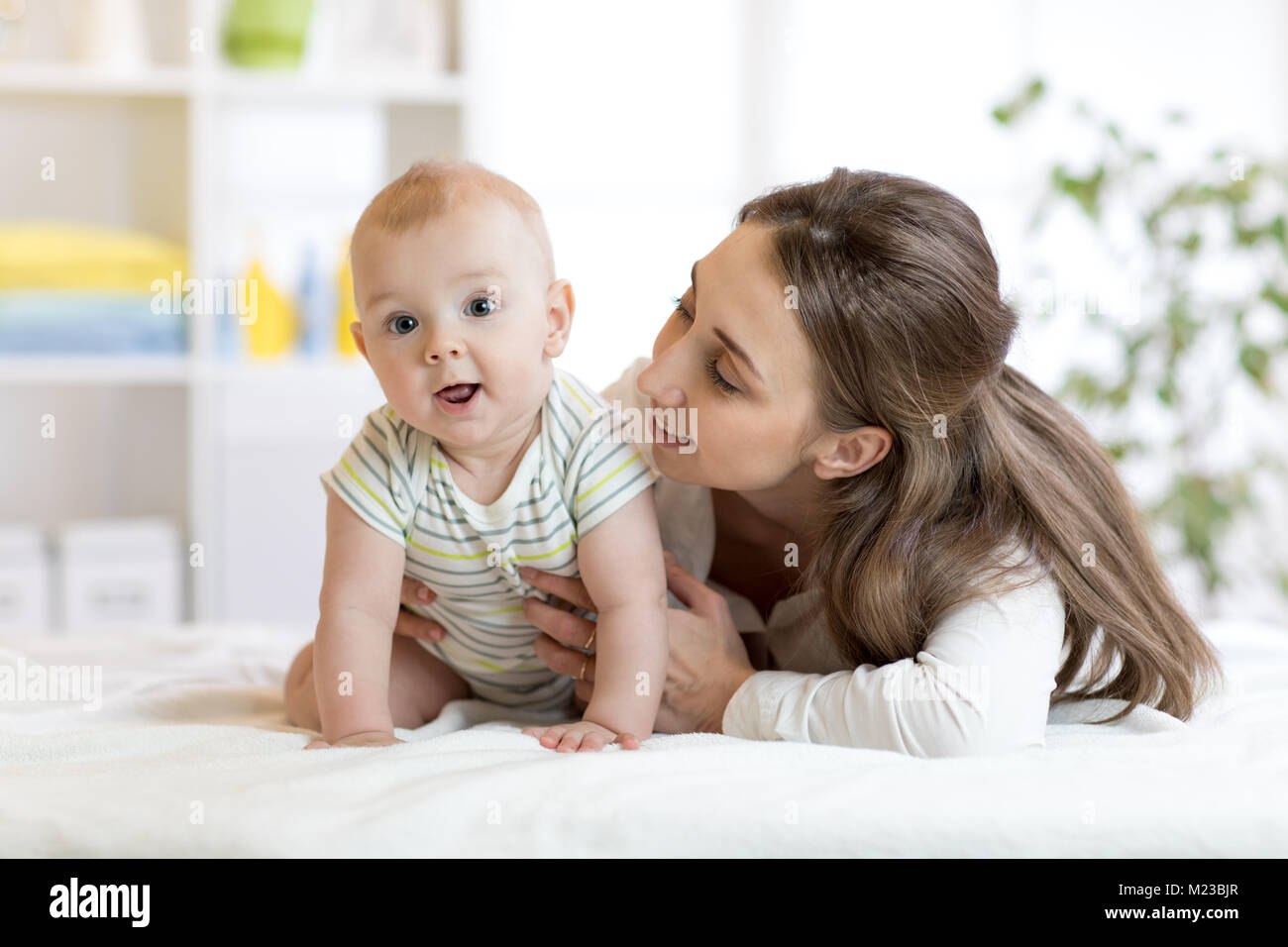 Mom looks at little son on bed. Happy mother embracing infant baby. Stock Photo