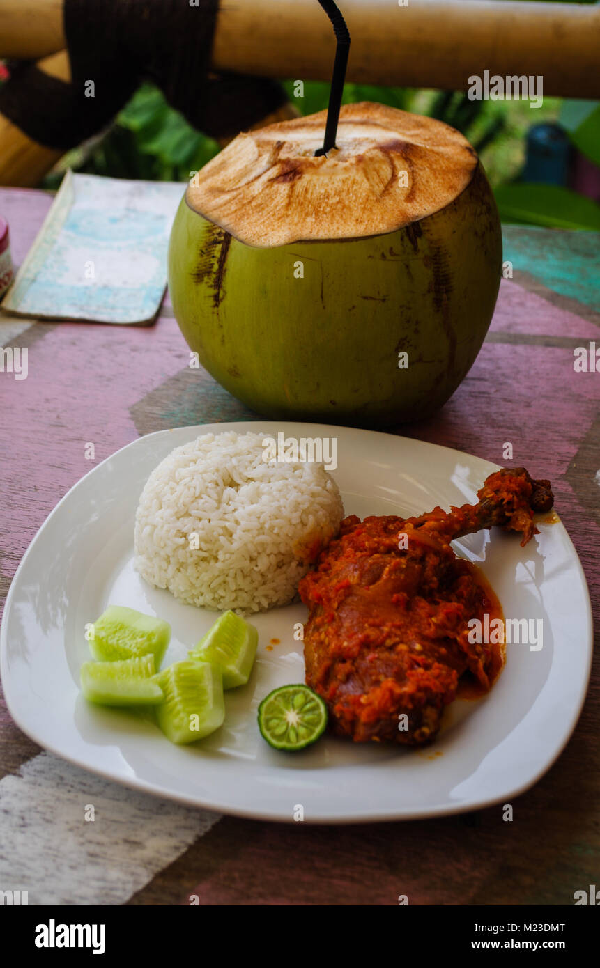 Typical Indonesian Dish: Nasi Ayam Plecing (Chicken with rice and special sauce) and young coconut vertical. Stock Photo