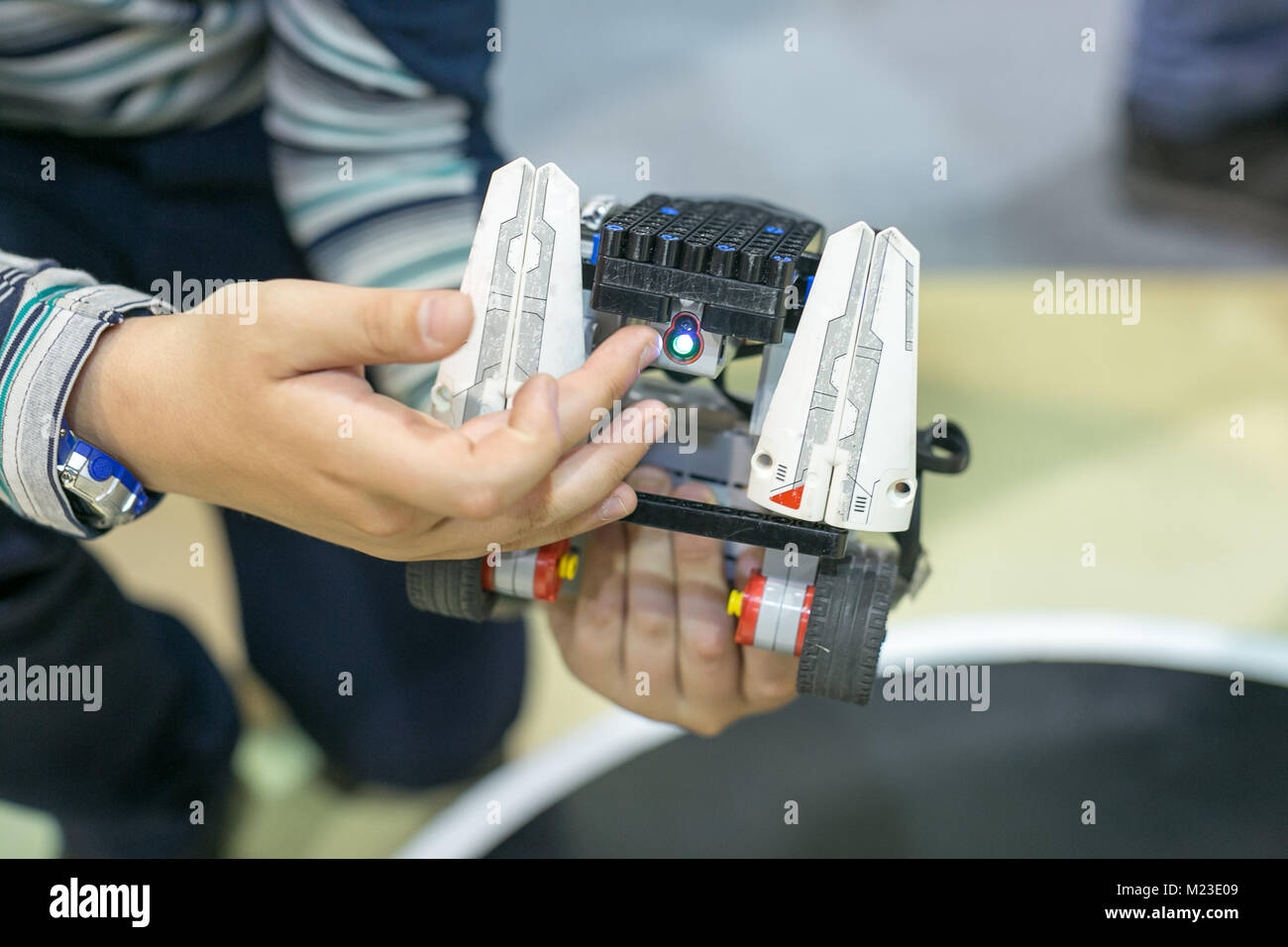 robotics, entertainment, childhood concept. in the arms of small boy there is robot made of lego parts, wheels and electric details for controlling it Stock Photo