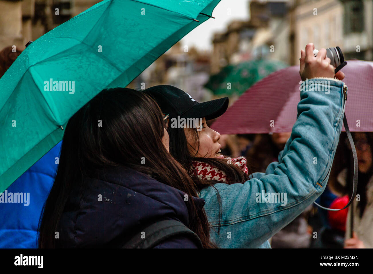 Two tourists taking a photograph on Cornmarket Street on a rainy day, Oxford, Oxfordshire, UK. Feb 2018 Stock Photo