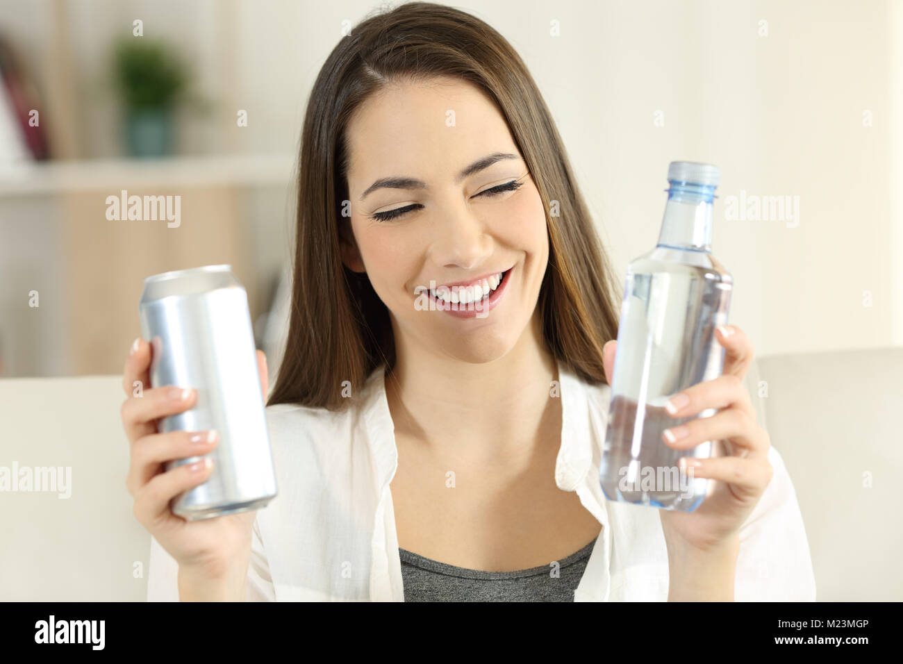 Front view portrait of a happy woman deciding between water or soda refreshment sitting on a couch in the living room at home Stock Photo