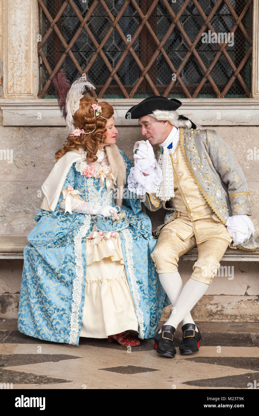 Venice Carnival 2018, Venice, Italy. Romantic couple in classical costumes sitting at the Doges Palace with the man kissing the womans hand Stock Photo