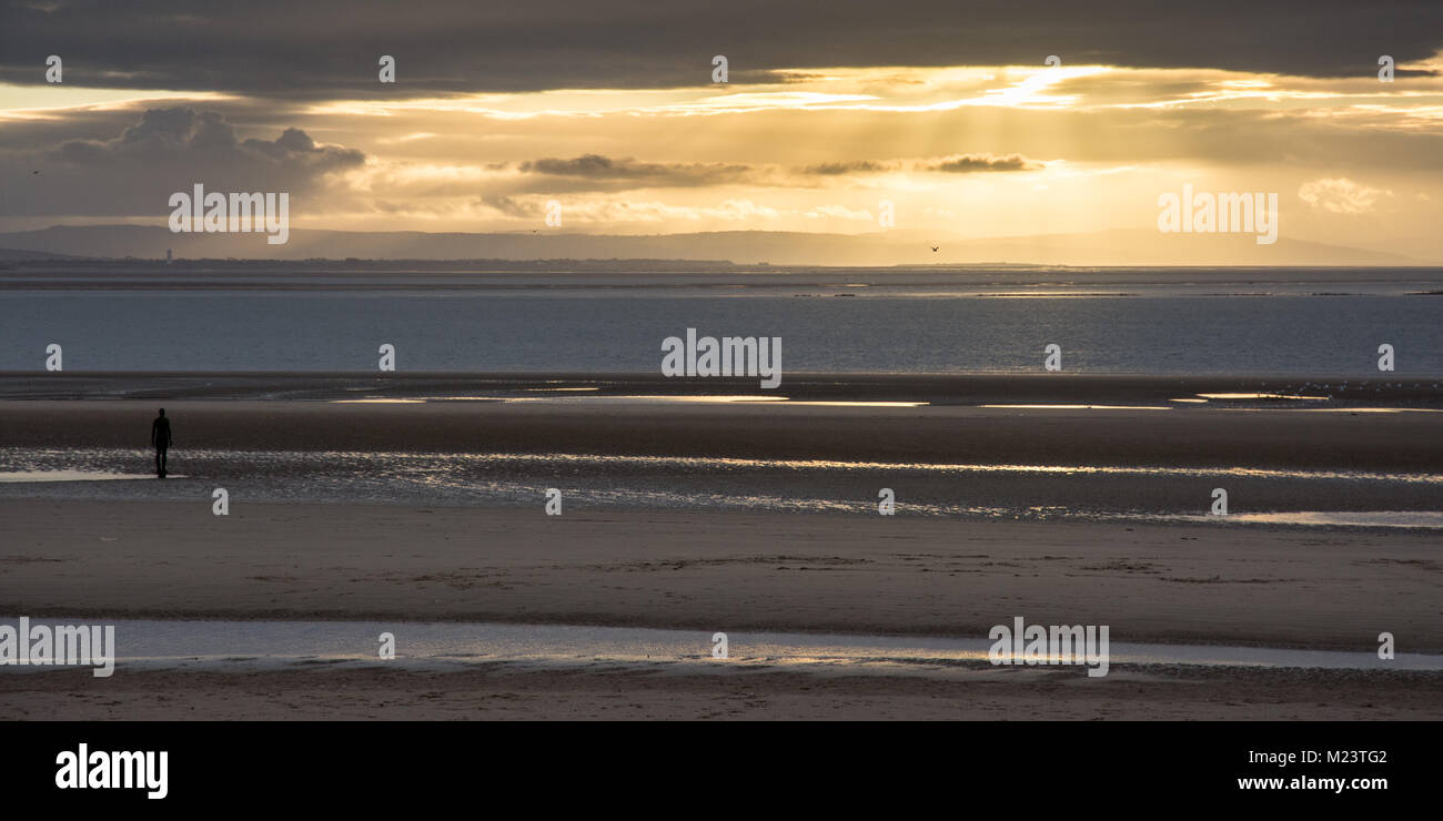 Liverpool, England, UK - November 12, 2016: The sun sets behind Antony Gormley's 'Another Place' sculptures on Crosby Beach, with the mountains of Sno Stock Photo