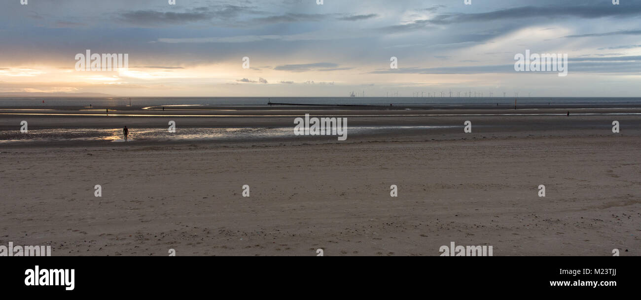 Liverpool, England, UK - November 12, 2016: The sun sets behind Antony Gormley's 'Another Place' sculptures on Crosby Beach, and wind farms and the Do Stock Photo