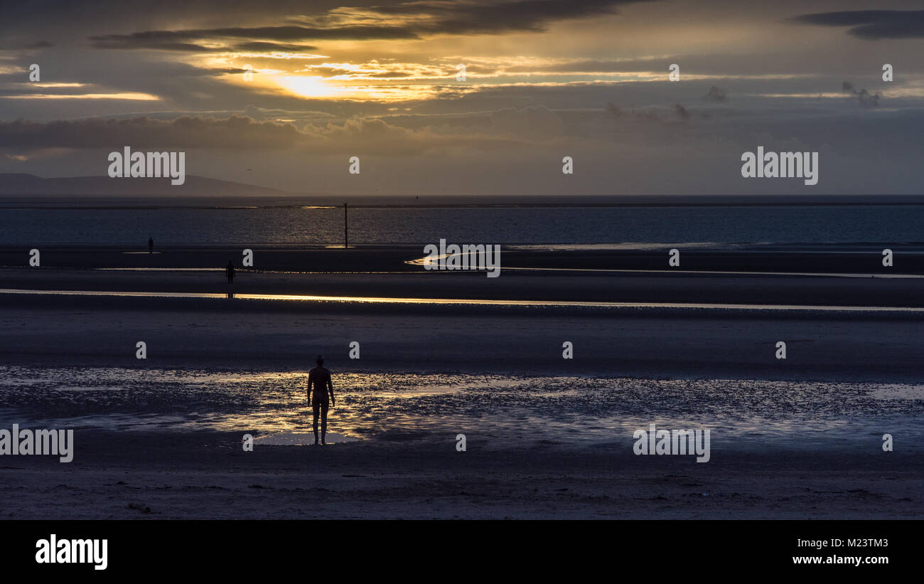 Liverpool, England, UK - November 12, 2016: The sun sets behind Antony Gormley's 'Another Place' sculptures on Crosby Beach, with the mountains of Sno Stock Photo
